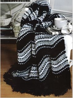 a black and white knitted blanket sitting on top of a table next to a cup