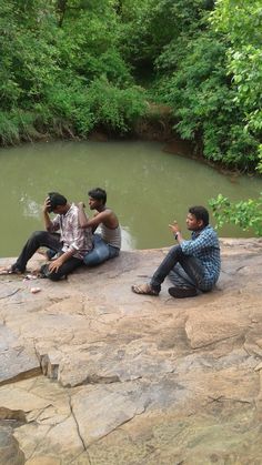 three people sitting on the edge of a river