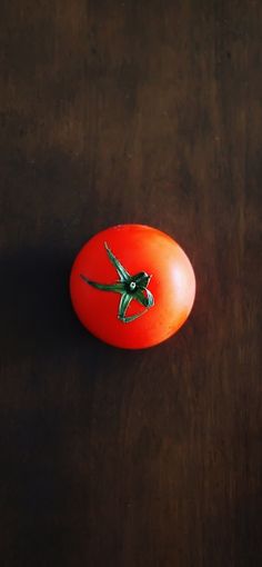 an orange tomato with a green bird painted on it's side sitting on a wooden surface