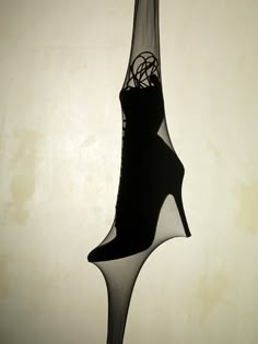 a black and white photo of a high heeled shoe hanging from a hook on a wall