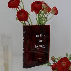 a red vase with flowers in it sitting next to a book that says un livve sur les fleurs