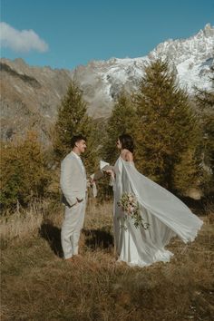 a bride and groom are standing in the mountains with their wedding dress blowing in the wind