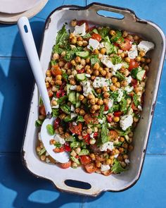 a white dish filled with salad sitting on top of a blue tile floor next to a spoon