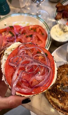 a person is holding up a sandwich with onions and tomatoes on it next to other food