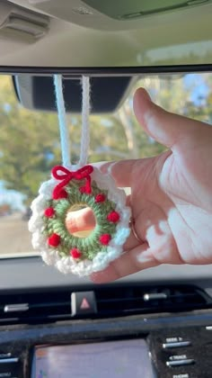 a hand holding a christmas wreath ornament hanging from the dashboard of a car