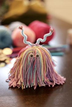 a close up of a tasseled object on a table with yarn balls in the background