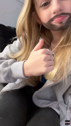 a man with long blonde hair wearing a fake moustache on his face and giving the thumbs up sign