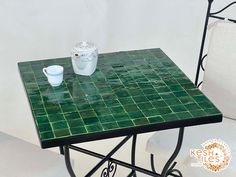 a green tiled table and chair with a cup sitting on top of it next to a white cushion