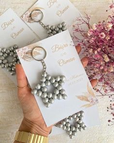 two cards with pearls are being held by someone's hand next to some flowers