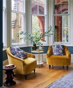 two chairs and a table in front of large windows with potted plants on them