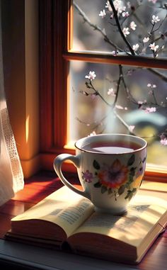 an open book sitting on top of a window sill next to a coffee cup