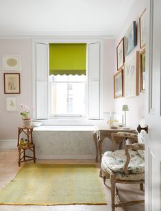 a white bath tub sitting under a window next to a chair and table with flowers on it