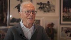 an older man wearing glasses standing in front of pictures