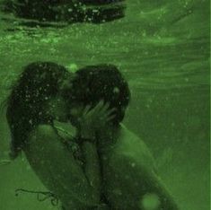 two people are kissing under the water with their arms around each other, and one person is swimming in the background