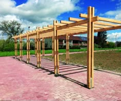 a row of wooden benches sitting on top of a pink brick walkway next to a lush green field