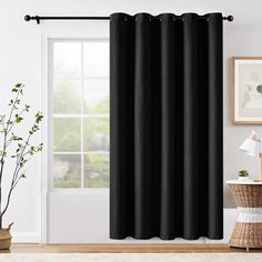 a black curtain hanging in front of a window with white walls and wooden flooring