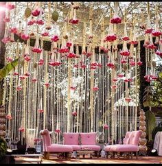 a decorated stage with pink couches and flowers hanging from it's ceiling for a wedding ceremony