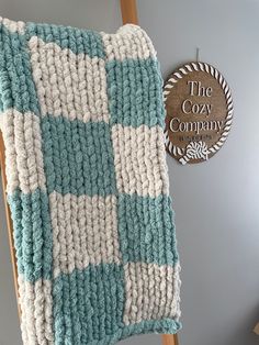 a blue and white knitted blanket hanging from a wooden hanger with the cozy company logo above it