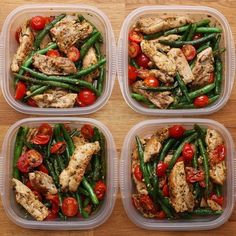 four plastic containers filled with chicken, green beans and cherry tomatoes on top of a wooden table