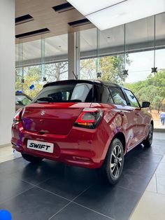 the rear end of a red suzuki swift parked in a showroom with large windows