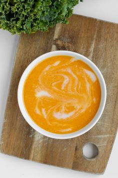 a bowl of carrot soup on a cutting board next to a leafy green plant