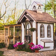 a small white and brown house with flowers in the front yard, next to a shed