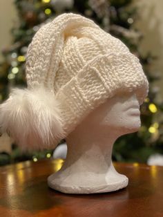 a white knitted hat sitting on top of a wooden table next to a christmas tree