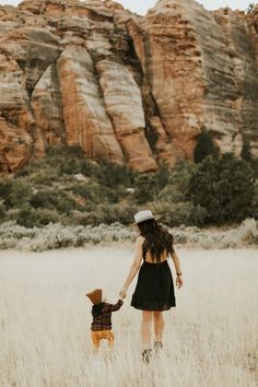 a woman holding the hand of a small child in a field with mountains in the background