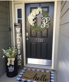 a black door with a welcome mat and white flowers