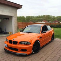 an orange bmw is parked in front of a garage with its door open and it's hood up