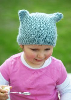 a small child wearing a knitted hat with ears and holding a spoon in their hand