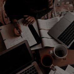 a person sitting at a table with two laptops and papers on top of it