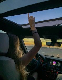 a woman is sitting in the passenger seat of a car and waving at the sunset