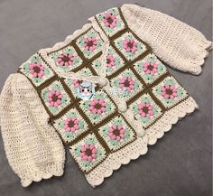 a crocheted sweater and mitten set with flowers on the front is shown