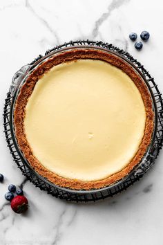 a cheesecake in a pie pan with fresh blueberries around it on a marble surface