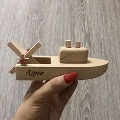 a hand holding a wooden model of a boat with the name aspen written on it