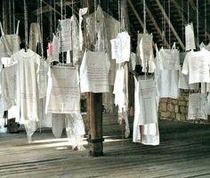 many white shirts hanging from the ceiling in a room with wooden floors and beams,