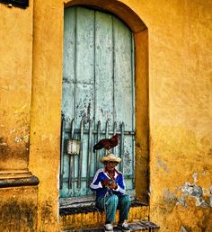 a person sitting on a step in front of a building with a bird perched on the door