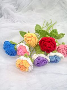 crocheted roses are arranged on a white surface with green stems and leaves in the center