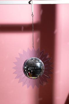 a disco ball hanging from a chain in front of a pink wall with mirrors on it