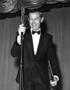 a black and white photo of a man in a tuxedo holding a microphone