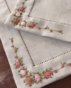 two white linens with pink roses on them are sitting on a wooden table next to each other