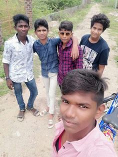 four young men standing on a dirt road with one man holding a bike in front of them