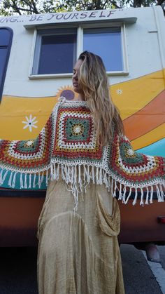 a woman standing in front of a bus with a crocheted shawl on her shoulders