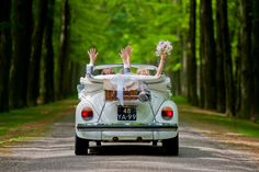 two people sitting in the back of a car with their hands up and holding flowers