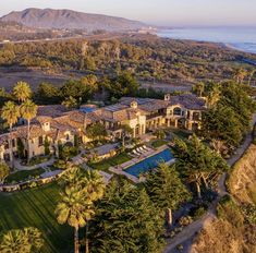 an aerial view of a mansion surrounded by palm trees and mountains in the distance is shown