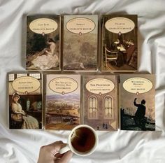 a person holding a cup of coffee in front of four books on a white sheet