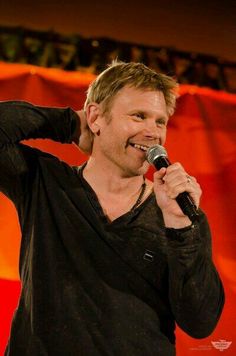 a man holding a microphone up to his ear while standing in front of a red curtain