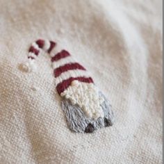 a knitted christmas ornament laying on top of a white blanket with red and gray stripes