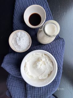 two bowls of whipped cream and one bowl of chocolate syrup on a blue towel with a cup of coffee next to it